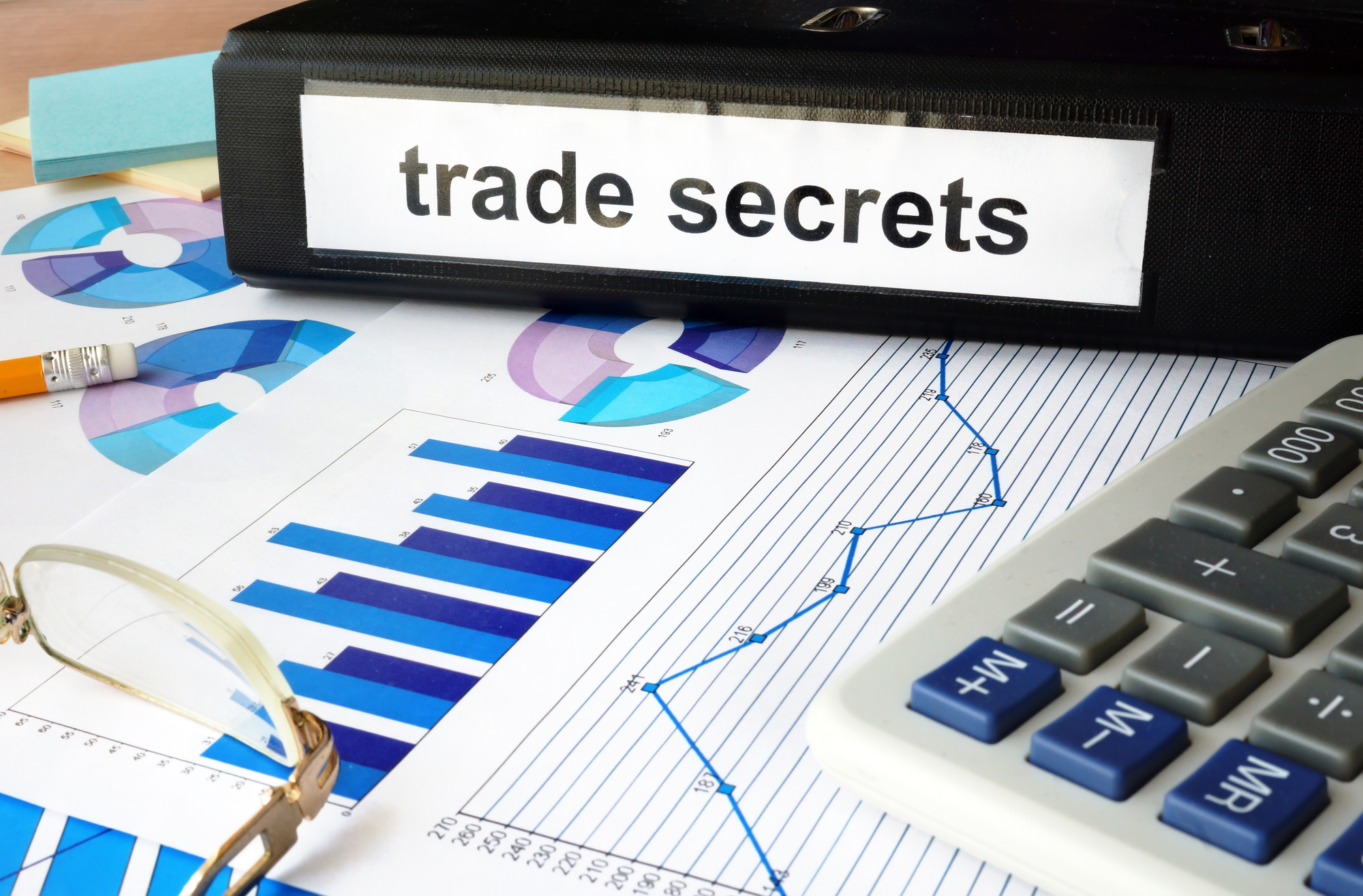 Still image: Binder labeled "trade secrets" resting on top of business papers and graphs.